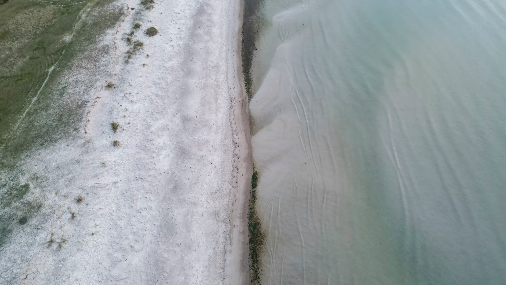 Dronefoto lige ned på kystlinje med turkis vand og hvidt sand